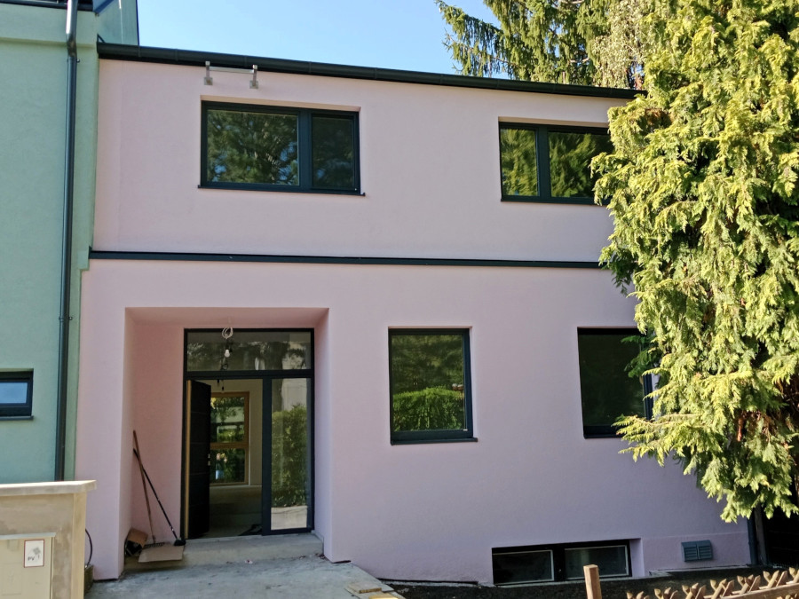 Modern saniertes, zweistöckiges Wohnhaus mit weißen Fassade, dunklen Fensterrahmen und einem überdachten Eingangsbereich.