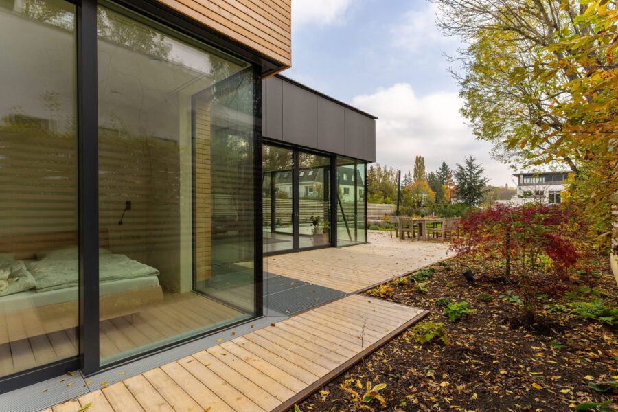 Modernes Einfamilienhaus in Holzbauweise mit großen Glasfronten, einer Holzterrasse und einem begrünten Garten.